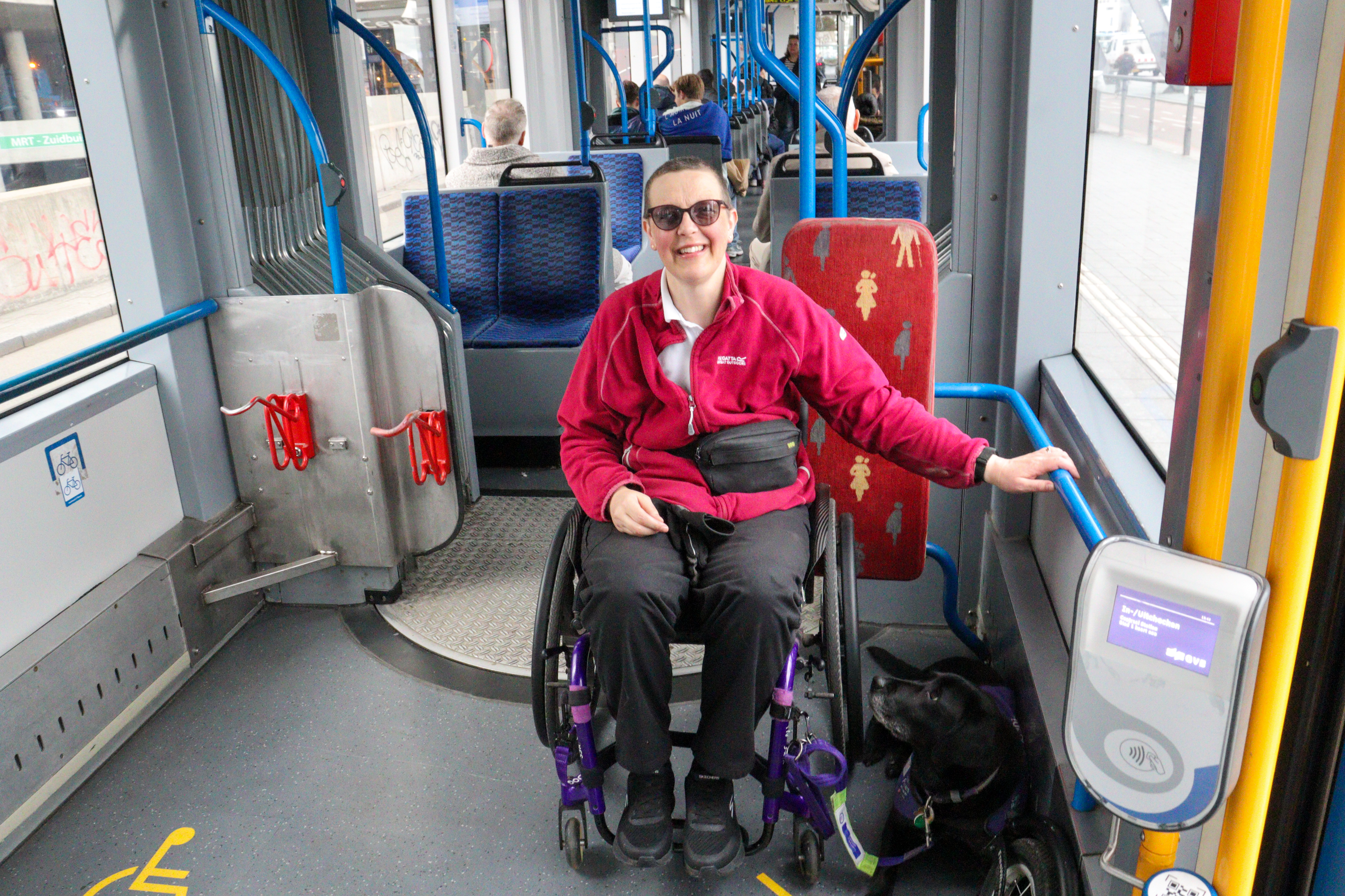 Lady in wheelchair on a tram, with black lab assistance dog lying next to her.