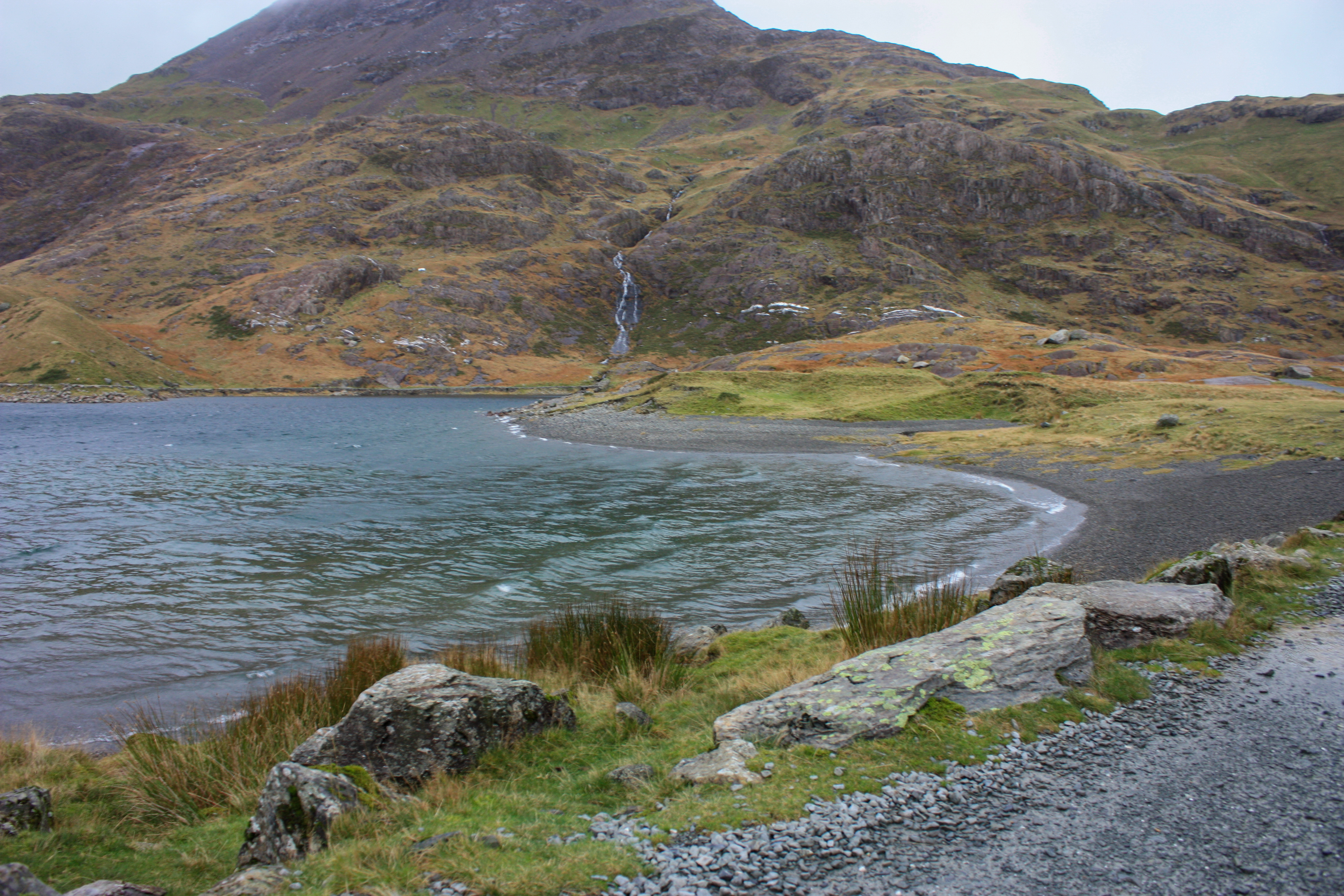 View of shoreline and mountain ahead with thin waterfall coming down into the lake.